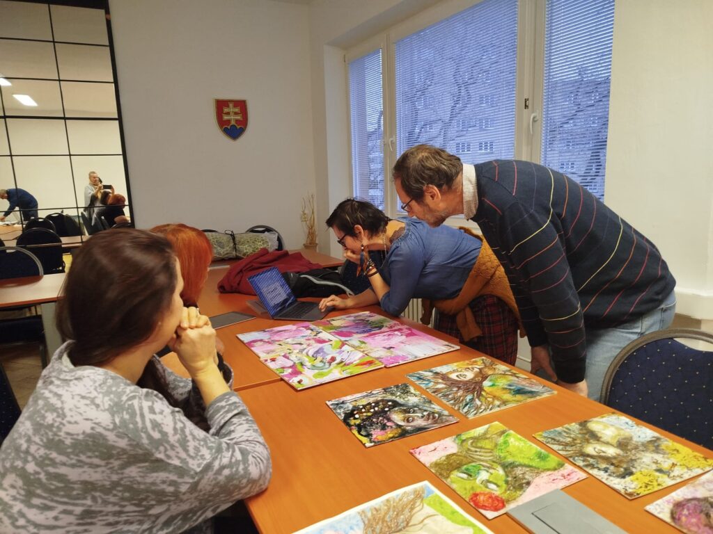 Tri ženy a jeden muž konzultujú výtvarné diela. 