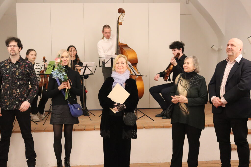 Kurátorka výstavy a dve ďalšie umelkyne stoja a usmievajú sa. 