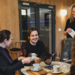 Jeden muž a dve ženy smejúci sa v kaviarni.