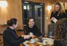 Jeden muž a dve ženy smejúci sa v kaviarni.