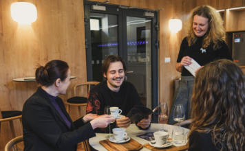 Jeden muž a dve ženy smejúci sa v kaviarni.